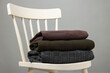 Stack of different warm sweaters on white chair against grey background