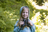 Fototapeta Kwiaty - Cute little girl exploring nature looking through binoculars. Child playing outdoors. Kids travel, adventure and bird watching concept.	