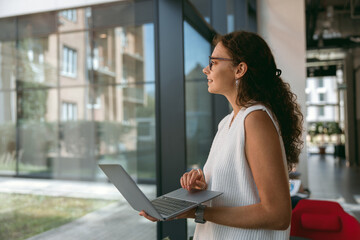 Stylish business woman working on laptop while standing on office background. High quality photo