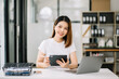 © Nuttapong punna - Young woman typing on tablet and laptop while sitting at the working wooden table modern office