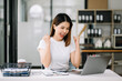 © Nuttapong punna - Young woman typing on tablet and laptop while sitting at the working wooden table modern office