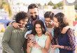 Group of young friends laughing by watching mobile phone during evening party gathering - concept of social media sharing, entertainment and friendship