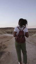 Vertical Back View Of A Young African Woman Walking On A Remote Location On Sunset In Countryside. Cheerful Girl On Nature Enjoy Her Summer Holidays Female Traveller Outdoors Desert Of Bardenas Reales