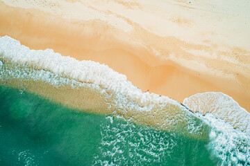 Aerial view of sandy beach and turquoise ocean. Top view of ocean waves reaching shore on sunny day.