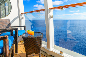 Two tropical mixed alcohol drinks sit on a small end table on the balcony veranda of a cruise ship stateroom on a sunny day on the Mediterranean Sea.