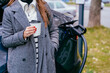 Eco friendly rechargeable EV car concept. Young woman in strip sweater standing with coffee to go, waiting for her electric car to charge on a public charging station outdoors.