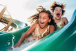 © larrui - Two child are going down a green water slide, their hair flying in the wind, against a backdrop of blue sky, creating a sense of fun and excitement, ai generative