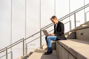 Wall Mural - Businessman sitting on steps outdoors using laptop