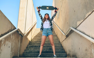 Sticker - Portrait of happy young woman standing on staircase holding up her longboard