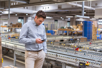 Wall Mural - Man at conveyor belt in factory looking at cell phone