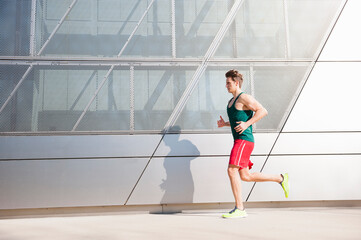 Mid adult man running on sidewalk by modern building in city