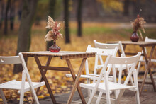 Autumn Outdoor Terrace With Wooden Table, Chairs And Decorations. Autumnal Street Scene In Park With Fallen Leaves. Street View Of A Coffee Terrace With Tables And Chairs In Europe.