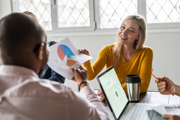 Smiling young businesswoman handing over document in a meeting