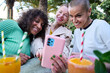 © CarlosBarquero - Three middle aged multiracial women pose smiling funny for selfie with mobile. Happy group of mature female friends using cell phone sitting on terrace of pub bar. Positive friendship relationships