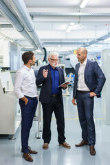 Wall Mural - Male colleagues listening to senior manager during discussing while standing at illuminated factory