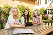 © tunedin - Three women of different age sitting at garden table using tablet