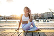 Asian woman practicing yoga on a pier at harbour, half-spinal twist at sunset