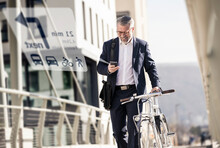 Smiling mature businessman with bicycle using cell phone for navigation in the city