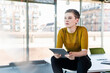 © tunedin - Thoughtful businesswoman sitting on desk in office holding tablet