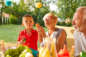 Wall Mural - Grandmother and grandson blowing soap bubbles on a garden party