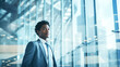 © EVGENIA - A young Afro businessman stands poised in a modern office setting, exuding confidence and professionalism amid the sleek glass surroundings