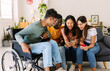 © Xavier Lorenzo - Diverse group of young friends laughing using mobile phone together at home. Inclusion concept with young indian man in wheelchair having fun with friends watching social media content on cell
