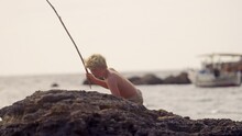 Boy Walking On Rocky Shore With Fishing Stick
