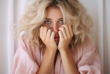 Closeup Of A Blonde Woman With Her Hands Over Her Face In Light Pink Sweater, Feeling Frightened, Sad.
