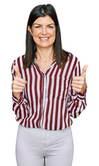 Wall Mural - Beautiful brunette woman wearing striped shirt success sign doing positive gesture with hand, thumbs up smiling and happy. cheerful expression and winner gesture.