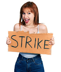 Sticker - Redhead young woman holding strike banner cardboard celebrating crazy and amazed for success with open eyes screaming excited.