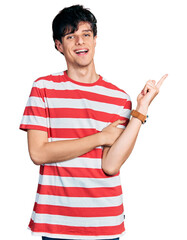 Poster - Handsome hipster young man wearing casual striped t shirt with a big smile on face, pointing with hand and finger to the side looking at the camera.