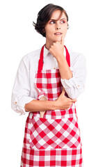 Poster - Beautiful young woman with short hair wearing professional cook apron with hand on chin thinking about question, pensive expression. smiling with thoughtful face. doubt concept.