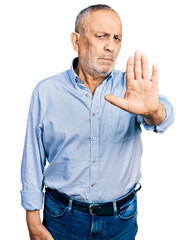 Wall Mural - Senior man with grey hair and beard wearing casual blue shirt doing stop sing with palm of the hand. warning expression with negative and serious gesture on the face.