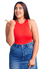 Poster - Young beautiful brunette woman wearing casual sleevelss t-shirt smiling with happy face looking and pointing to the side with thumb up.