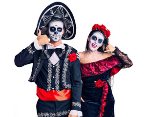 Wall Mural - Young couple wearing mexican day of the dead costume over background smiling doing phone gesture with hand and fingers like talking on the telephone. communicating concepts.