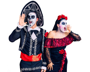 Canvas Print - Young couple wearing mexican day of the dead costume over background shouting and screaming loud to side with hand on mouth. communication concept.