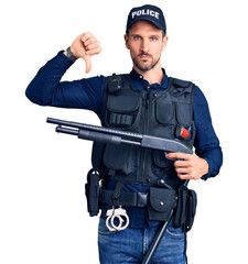 Poster - Young handsome man wearing police uniform holding shotgun with angry face, negative sign showing dislike with thumbs down, rejection concept