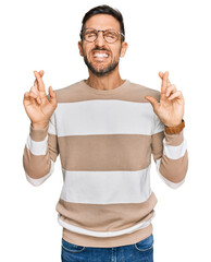 Canvas Print - Handsome man with beard wearing casual clothes and glasses gesturing finger crossed smiling with hope and eyes closed. luck and superstitious concept.