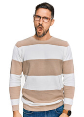 Sticker - Handsome man with beard wearing casual clothes and glasses in shock face, looking skeptical and sarcastic, surprised with open mouth