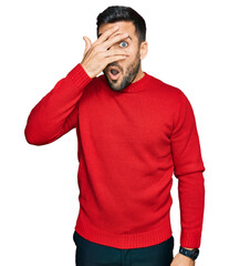 Sticker - Young hispanic man wearing casual clothes peeking in shock covering face and eyes with hand, looking through fingers with embarrassed expression.