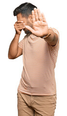 Sticker - Handsome hispanic man wearing casual clothes covering eyes with hands and doing stop gesture with sad and fear expression. embarrassed and negative concept.