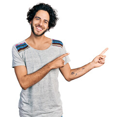 Sticker - Young hispanic man wearing casual t shirt smiling and looking at the camera pointing with two hands and fingers to the side.