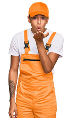 Canvas Print - Young handsome african american man wearing handyman uniform looking at the camera blowing a kiss with hand on air being lovely and sexy. love expression.