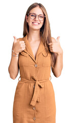 Wall Mural - Young beautiful blonde woman wearing casual clothes and glasses success sign doing positive gesture with hand, thumbs up smiling and happy. cheerful expression and winner gesture.