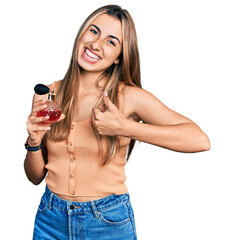 Canvas Print - Hispanic young woman holding perfume smiling happy and positive, thumb up doing excellent and approval sign