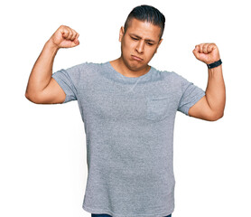 Wall Mural - Young latin man wearing casual clothes showing arms muscles smiling proud. fitness concept.