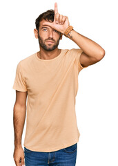 Canvas Print - Handsome young man with beard wearing casual tshirt making fun of people with fingers on forehead doing loser gesture mocking and insulting.