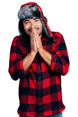 Canvas Print - Hispanic young man with beard wearing fluffy earmuff hat praying with hands together asking for forgiveness smiling confident.