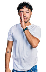 Wall Mural - Hispanic young man with beard wearing casual white t shirt hand on mouth telling secret rumor, whispering malicious talk conversation