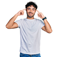 Poster - Hispanic young man with beard wearing casual white t shirt smiling pointing to head with both hands finger, great idea or thought, good memory